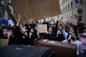- Revolutionary News Today! Crowd of Protesters in a City Street, Many Wearing Masks, Holding Up Protest Signs Including a Large Cardboard Sign.